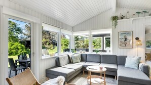 A modern living room with a grey sectional sofa, wicker furniture, and a large window overlooking greenery.