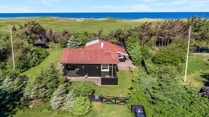 A house with a red roof, surrounded by greenery and a view of the ocean.