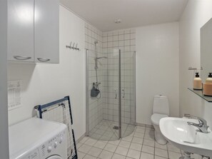 A modern bathroom with a glass-enclosed shower, a white sink, and a washing machine.