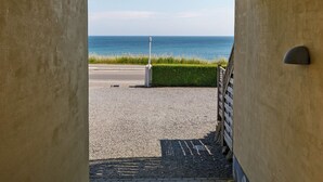 En vy genom en dörröppning mot ett belagt område med ett metallräcke och en gräsyta som leder ner till havet.