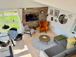 A modern living room with a large TV, a grey sofa, a round coffee table, and a dining area with a small table and chairs.
