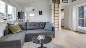 Un salon moderne avec un canapé d’angle gris, une table basse ronde et une échelle appuyée contre le mur.
