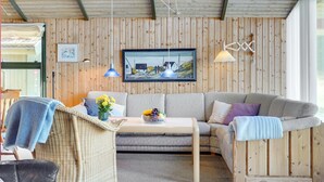 A cozy living room with a wooden ceiling, a grey sofa, a wicker chair, and a small table with a vase of flowers. - "Alfrik" - 900m from the sea by Interhome (Blokhus)