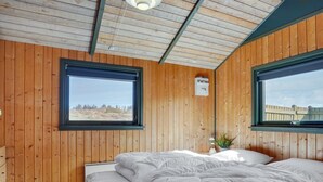 A room with wooden walls, a bed with white bedding, two windows, and a small plant on the windowsill. - "Alfrik" - 900m from the sea by Interhome (Blokhus)