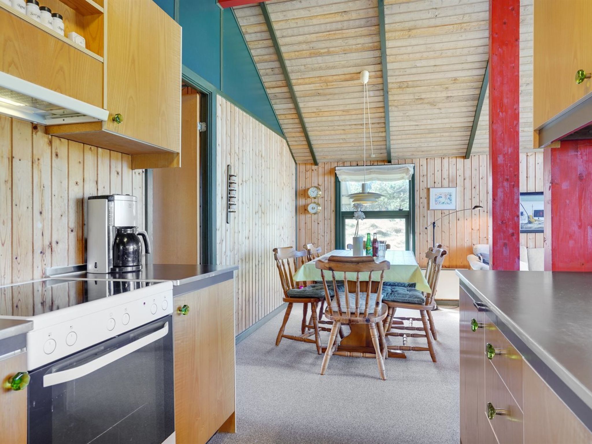 Una cucina moderna con rivestimenti in legno, un'area pranzo con tavolo e sedie, e una parete di accentazione rossa.