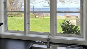 A kitchen with a window overlooking a grassy yard and a body of water. - "Zina" - 25m from the sea by Interhome (Gudhjem)