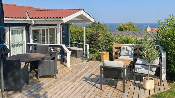 Een houten terras met buitenmeubilair, een overdekte zithoek en uitzicht op de zee.