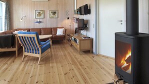 Een gezellige woonkamer met een houten vloer, een bank, een blauw gestreepte stoel, een tafel, een televisie en een houtkachel.