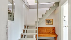 A staircase leading to a loft area with a skylight, a wooden bench, and a framed artwork on the wall.