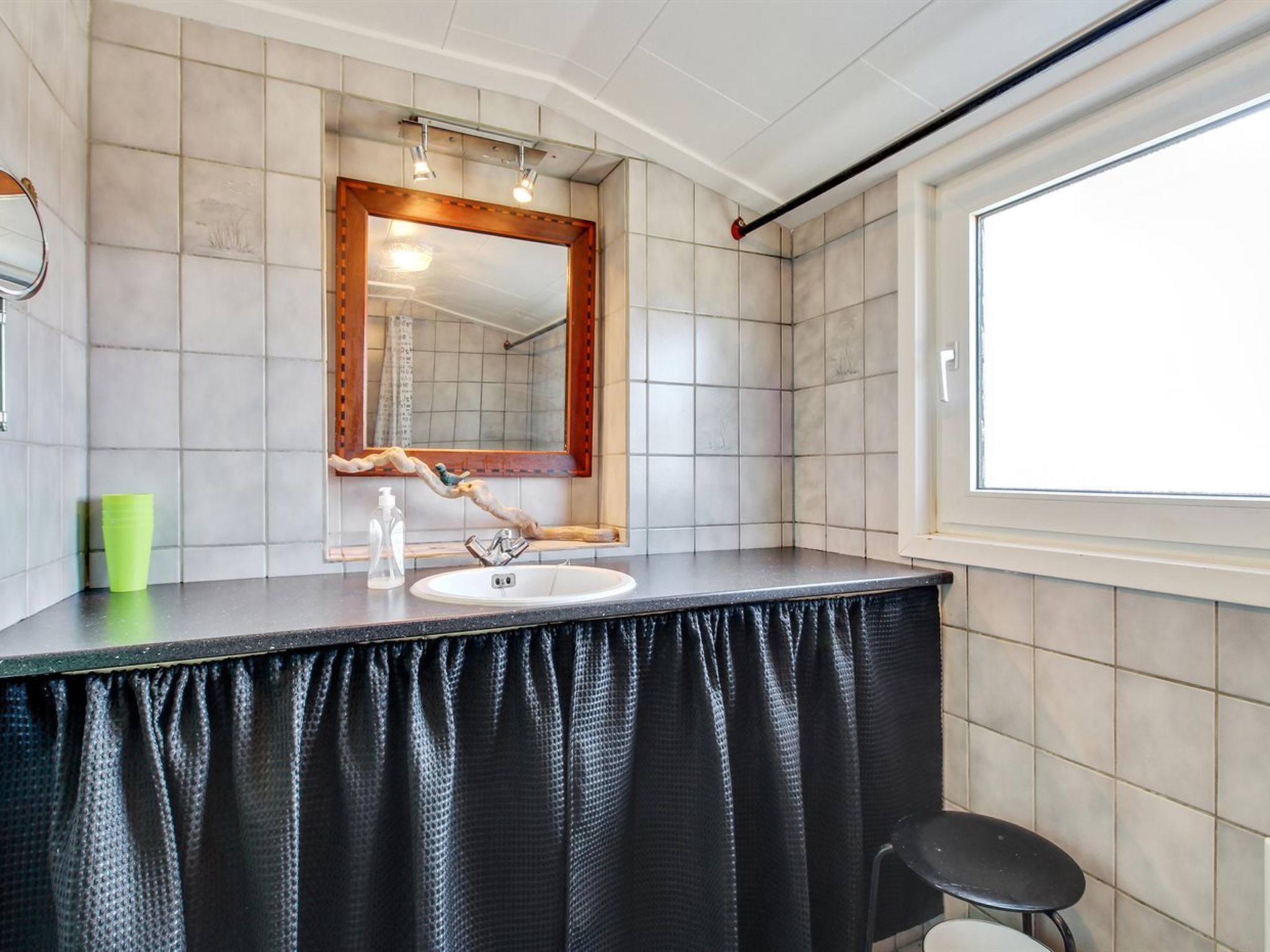 Ein Badezimmer mit schwarzem Waschtisch, weißem Waschbecken, einem spiegelnden Wandbild mit Holzrahmen und einem Fenster.