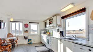 A modern kitchen with white cabinets, a large window, and a dining area with wicker chairs.