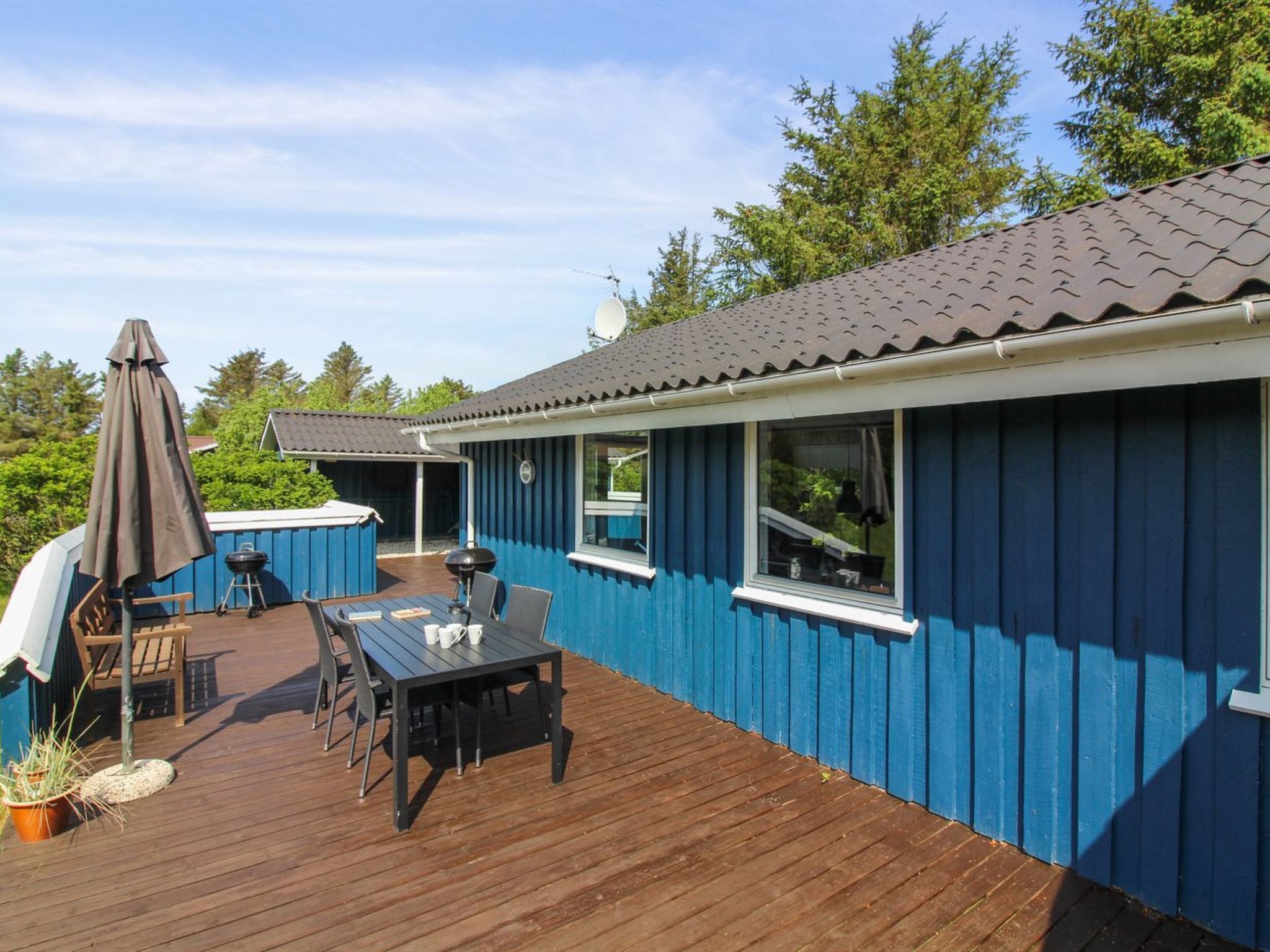 A blue wooden building with a deck, a barbecue grill, and outdoor seating.