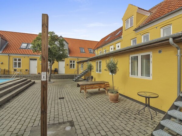 Ein Innenhof mit Swimmingpool, Holzbanken, einem kleinen Tisch und einer Treppe, die zu einer zweiten Etage führt.