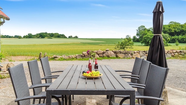 A wooden table with chairs and a fruit bowl, set outdoors with a stone wall and greenery in the background. - "Helmer" - 3km from the sea by Interhome (Østermarie)