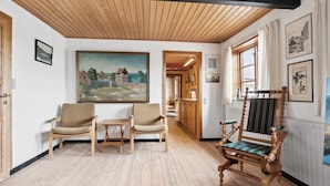 A room with wooden flooring, a painting on the wall, two chairs, a table, and a wooden bench with a cushion. - "Helmer" - 3km from the sea by Interhome (Østermarie)