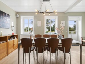 Een eethoek met een tafel voor zes personen, omringd door zes stoelen, en een moderne kroonluchter erboven.