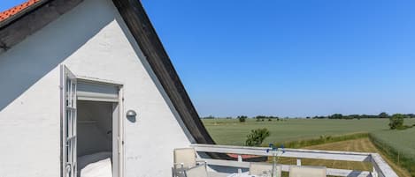 Un edificio blanco con una terraza de madera, una mesa con sillas y vistas a un campo verde.