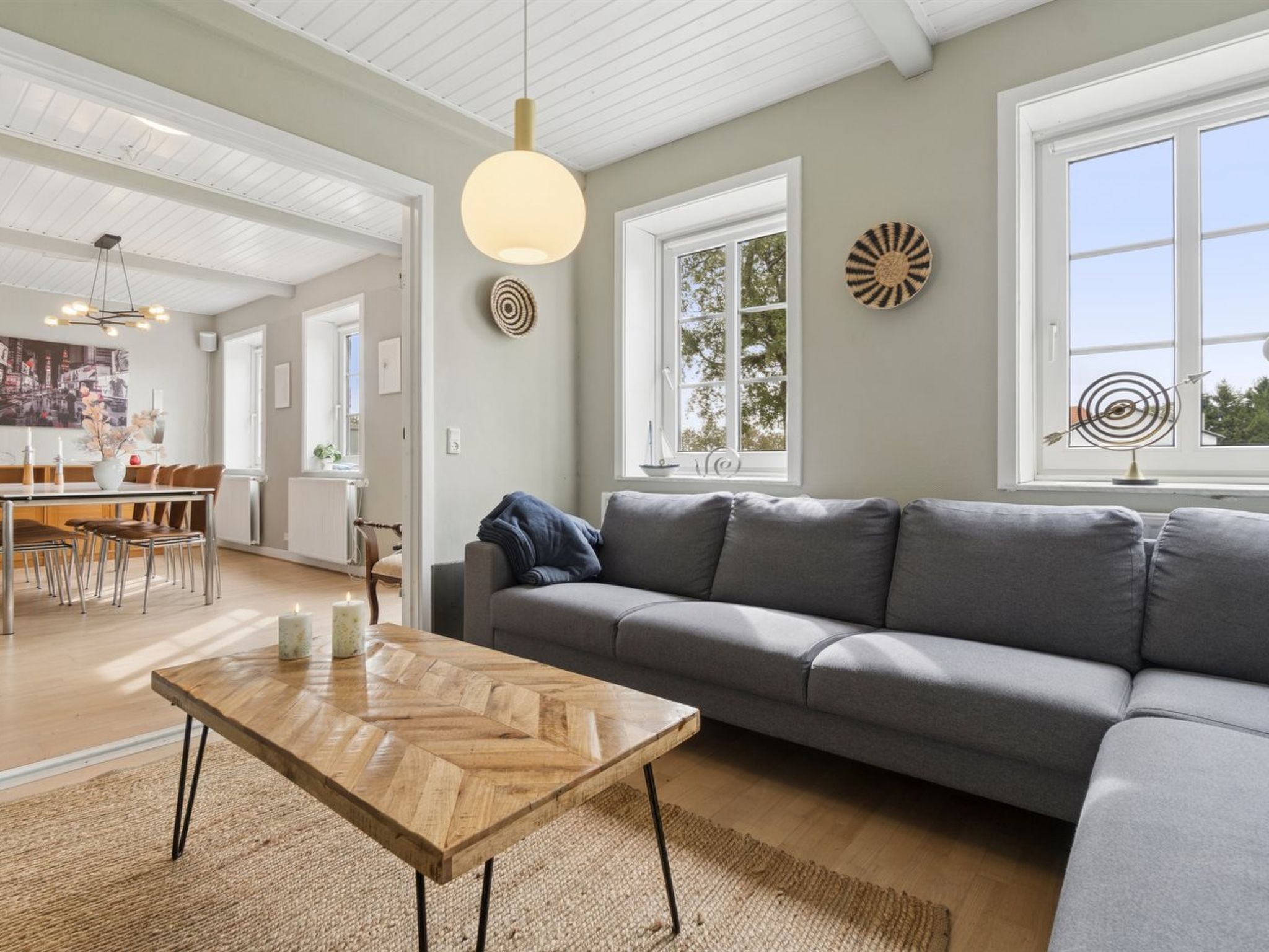 Una sala de estar moderna con un sofá gris, una mesa de centro de madera y una lámpara colgante.