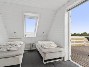 A small, white, attic-style bedroom with two beds and a window.