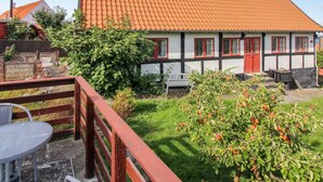 Ein traditionelles Fachwerkhäuschen mit rotem Ziegeldach, umgeben von einem gepflegten Garten mit Obstbäumen und einer Holzterrasse mit Gartenmöbeln.