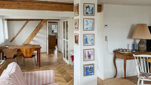 Ein gemütliches Wohnzimmer mit Holzboden, einem Essbereich mit Tisch und Stühlen sowie einer Wand mit gerahmten Bildern.