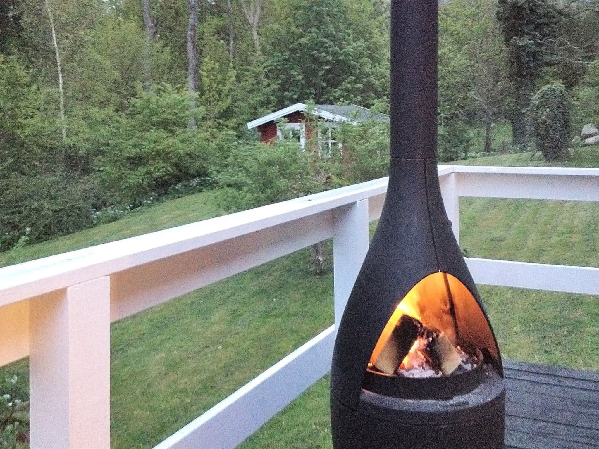 A deck with a black chimney emitting smoke, surrounded by a white railing and lush greenery.