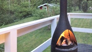 A deck with a black chimney emitting smoke, surrounded by a white railing and lush greenery.