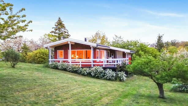 A red and white cabin with a porch, surrounded by a grassy field and trees.