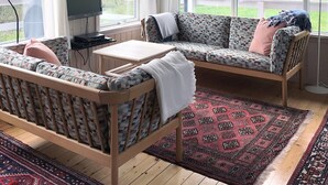 A cozy room with a sofa, a small table, and a TV. There are large windows with a view of a garden.