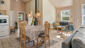 Une pièce spacieuse avec un plafond haut, des murs en bois, un coin repas avec une table dressée pour quatre personnes, un canapé et une cheminée.