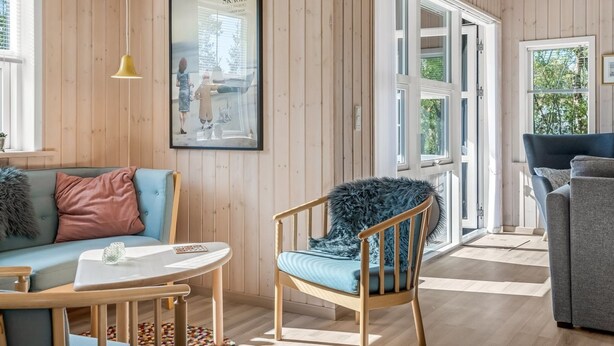 Une pièce aux murs recouverts de lambris en bois, avec un tableau encadré, un canapé bleu, une chaise en bois, une petite table et une fenêtre donnant sur un paysage.
