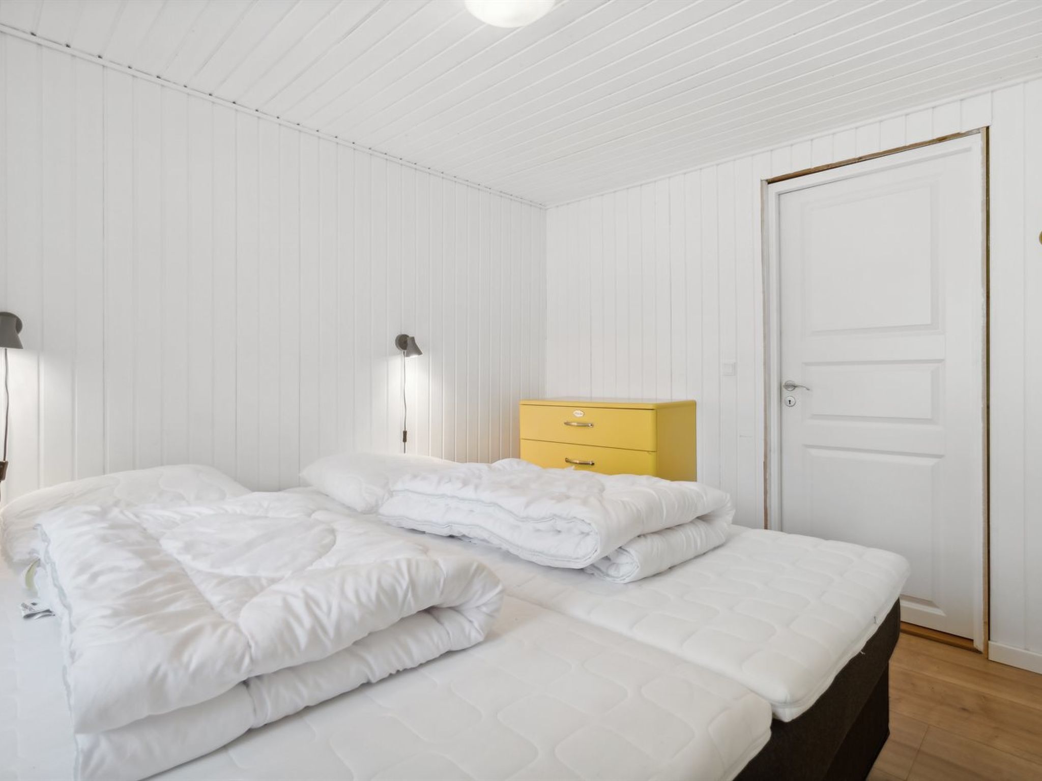 A bedroom with two beds, a yellow dresser, and a white door.