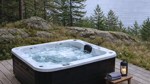 A hot tub on a wooden deck with a lantern and towels beside it, surrounded by a forest and a body of water. - "Ilmari" - 150m from the sea by Interhome (Nexø)