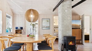 A cozy room with a round wooden table, six chairs, a hanging light fixture, a fireplace, and a view of the outdoors through a window. - "Ilmari" - 150m from the sea by Interhome (Nexø)