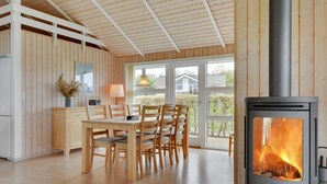 Una habitación acogedora con detalles de madera, un rincón de comedor con sillas, una mesa y un estufa de leña.