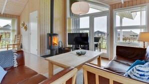 Una sala de estar acogedora con una estufa de leña, un televisor y un amplio ventanal con vistas al exterior.