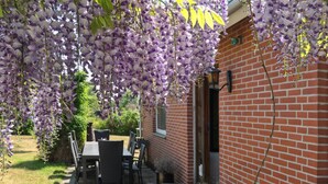 Un patio con pared de ladrillo, mobiliario exterior y flores moradas colgantes.