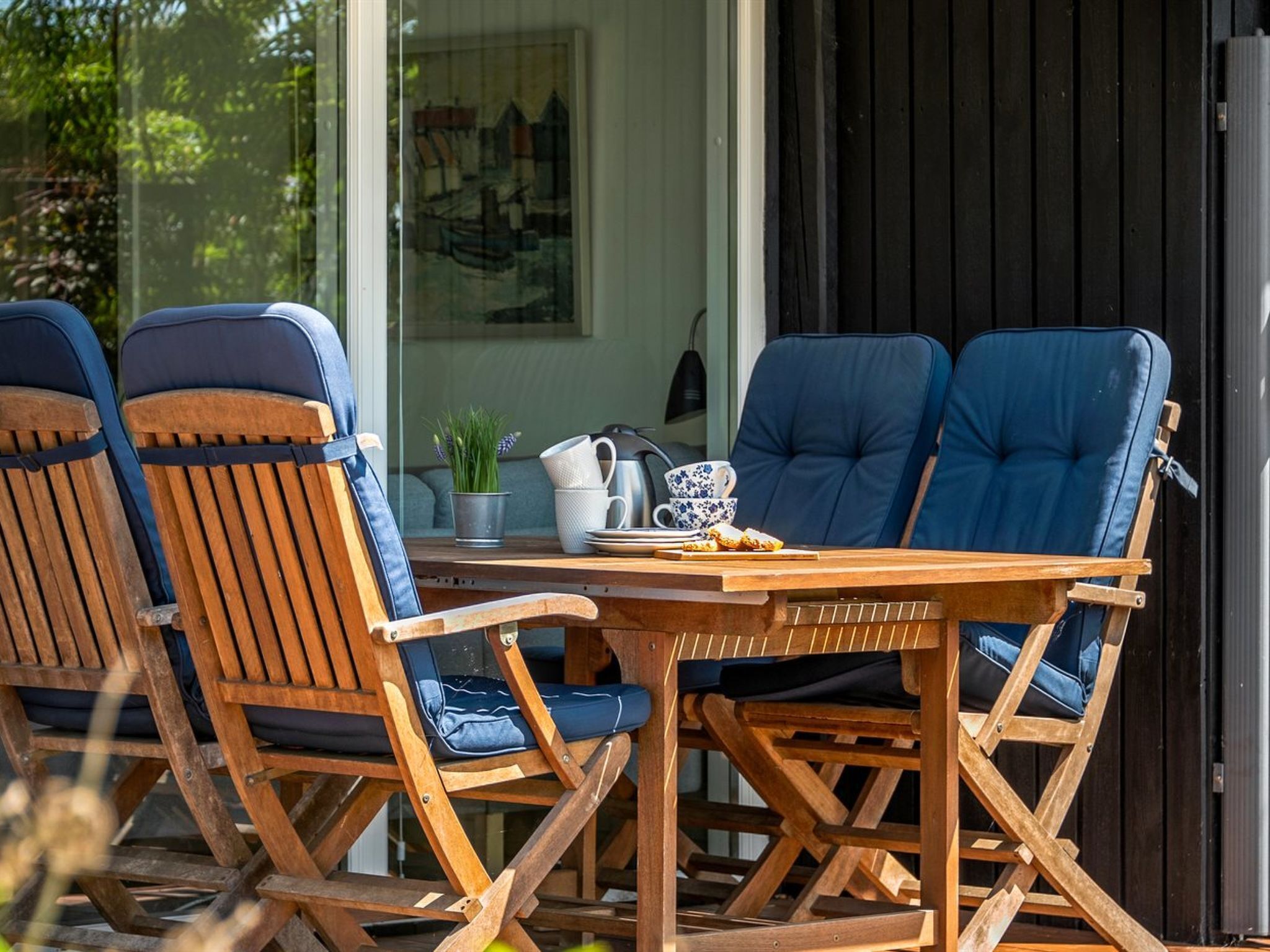 A wooden table with blue cushioned chairs, a white pitcher, a blue and white cup, and a small potted plant.