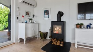Une pièce dotée d’un poêle à bois, de meubles blancs et d’une grande fenêtre.