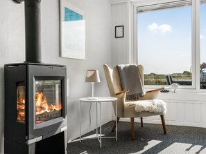 Een kamer met een houtkachel, een stoel, een klein tafeltje en een raam met uitzicht.