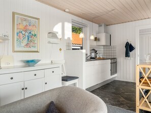 Een moderne keuken met witte kasten, een zithoek met een grijze bank en een schilderij aan de muur.