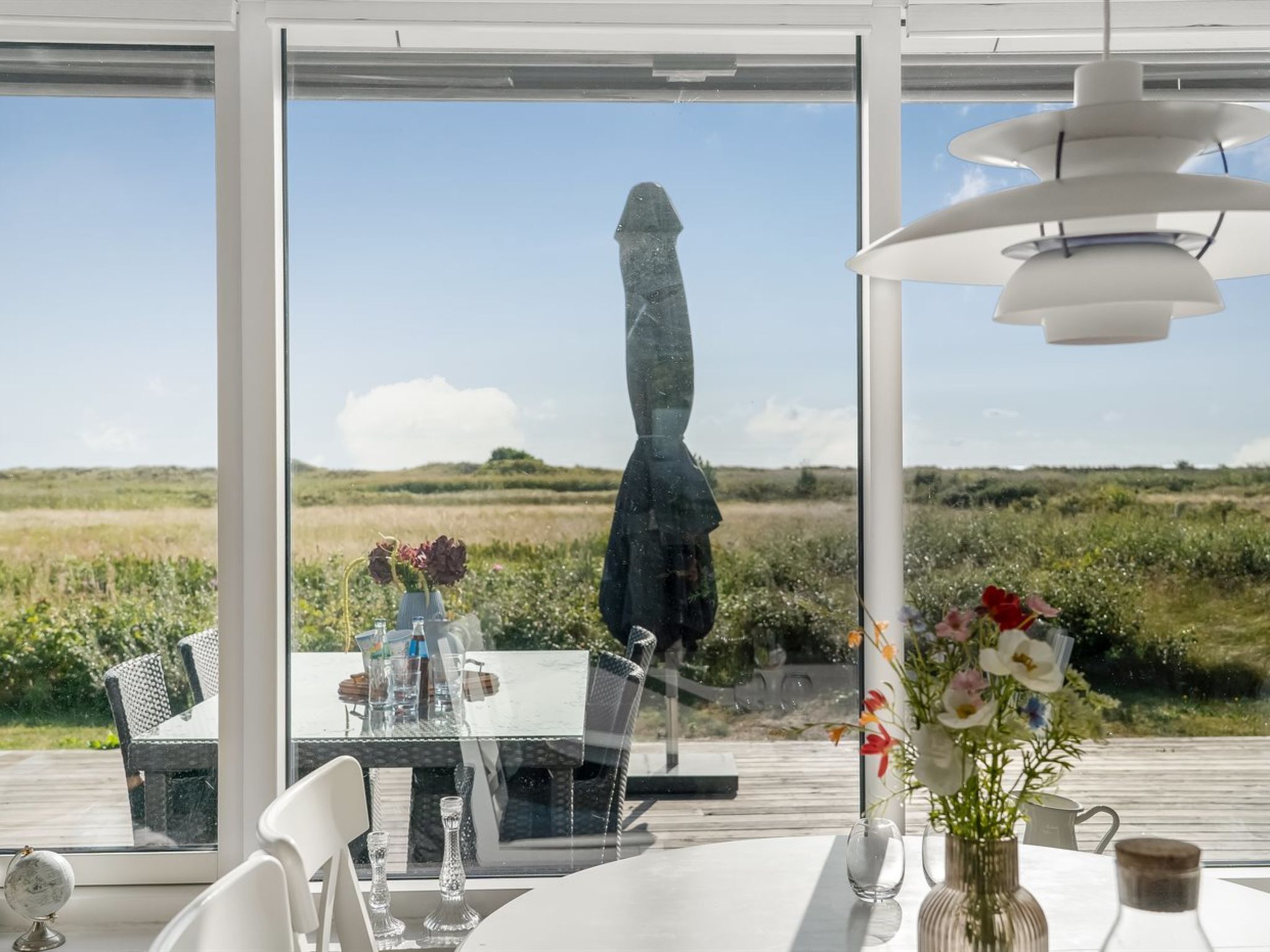Un coin repas avec une table dressée pour deux personnes, un globe terrestre et une vue sur un paysage côtier, visible à travers de grandes fenêtres.