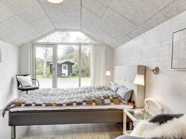 A bedroom with a large bed, a chair, a bedside table, and a view of a house through a window. - "Mumme" - 100m from the sea by Interhome (Hals)