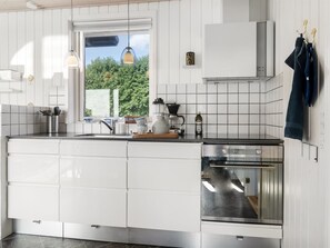 Une cuisine moderne avec des meubles blancs, un four encastré et une fenêtre donnant sur un paysage verdoyant.