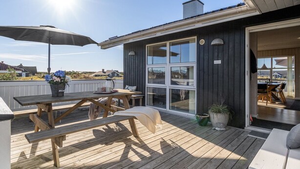 Un terrazza in legno con un tavolo e sedie, una pianta in vaso e vista sul paesaggio circostante.