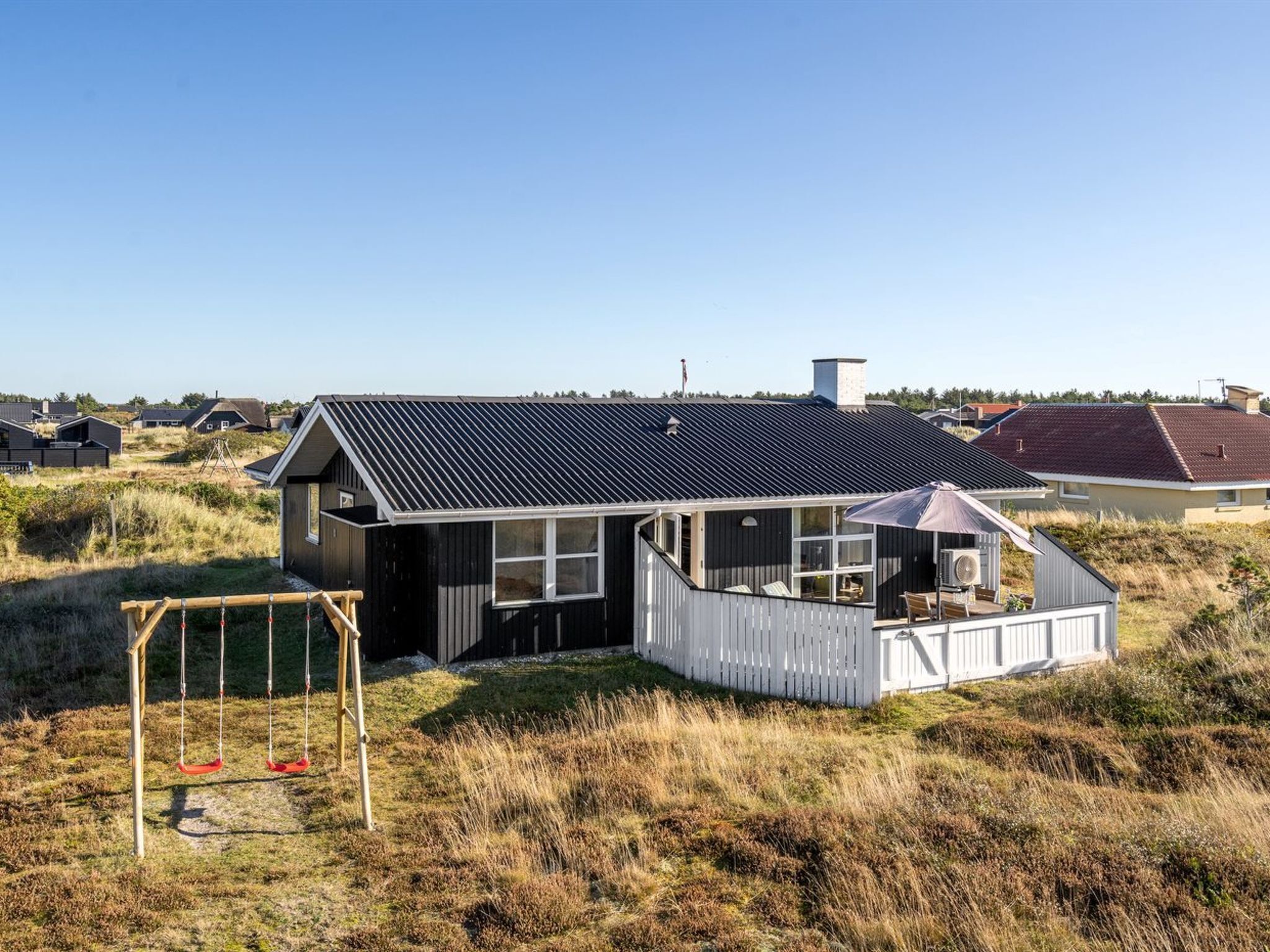 A modern house with a sloped roof, a fenced deck, and a swing set in the yard.