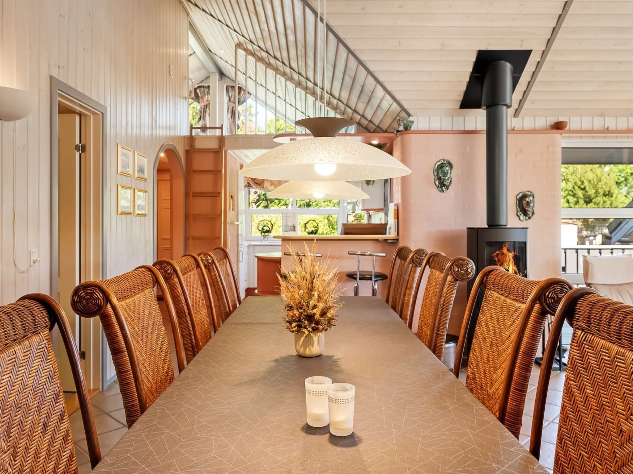 A long dining table with wicker chairs, a vase with dried flowers, and candles.