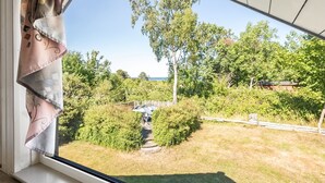 Ikkunasta avautuu näkymä puutarhaan, näkyy puinen aita ja kauempana oleva rakennus.