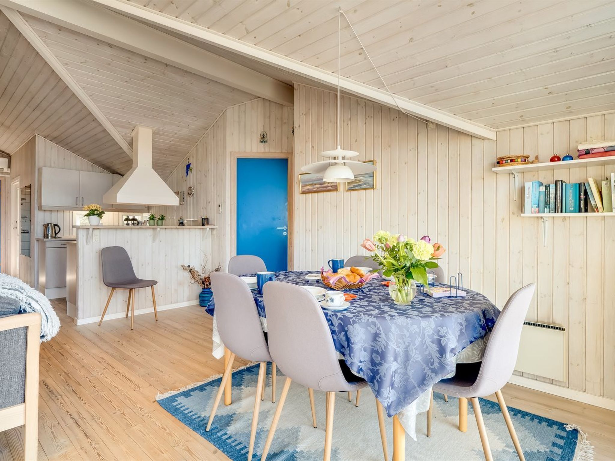 Une cuisine moderne avec des meubles en bois, une porte bleue et un coin repas avec une table dressée pour quatre personnes.