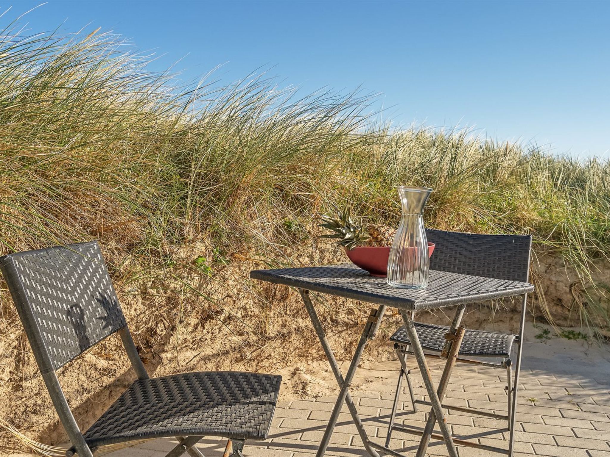 A beachside table and chairs with a woven chair design, a clear glass vase, and a bowl with a plant.